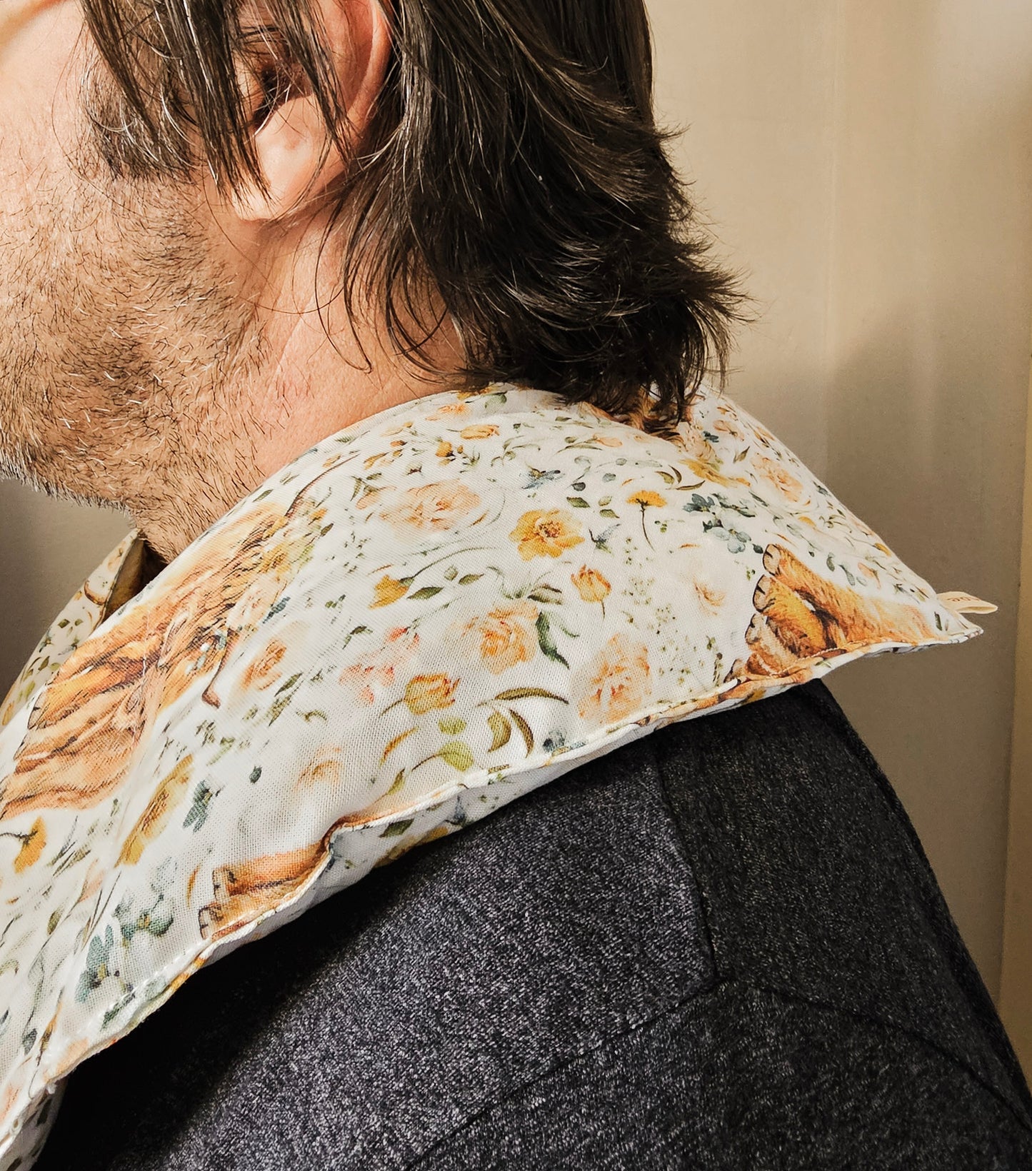 A close-up side view of a person wearing hot and cold neck packgreen, and brown tones on an off-white background, paired with a dark gray textured jacket.