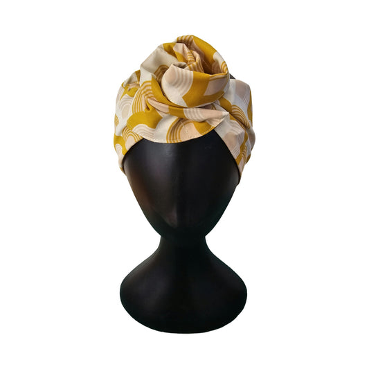 Yellow and beige patterned headwrap on a black mannequin head against a white background front view