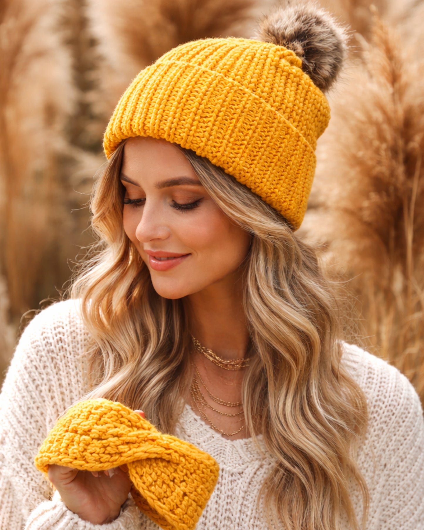 Woman wearing a yellow knit beanie and matching gloves in a field of tall grass.