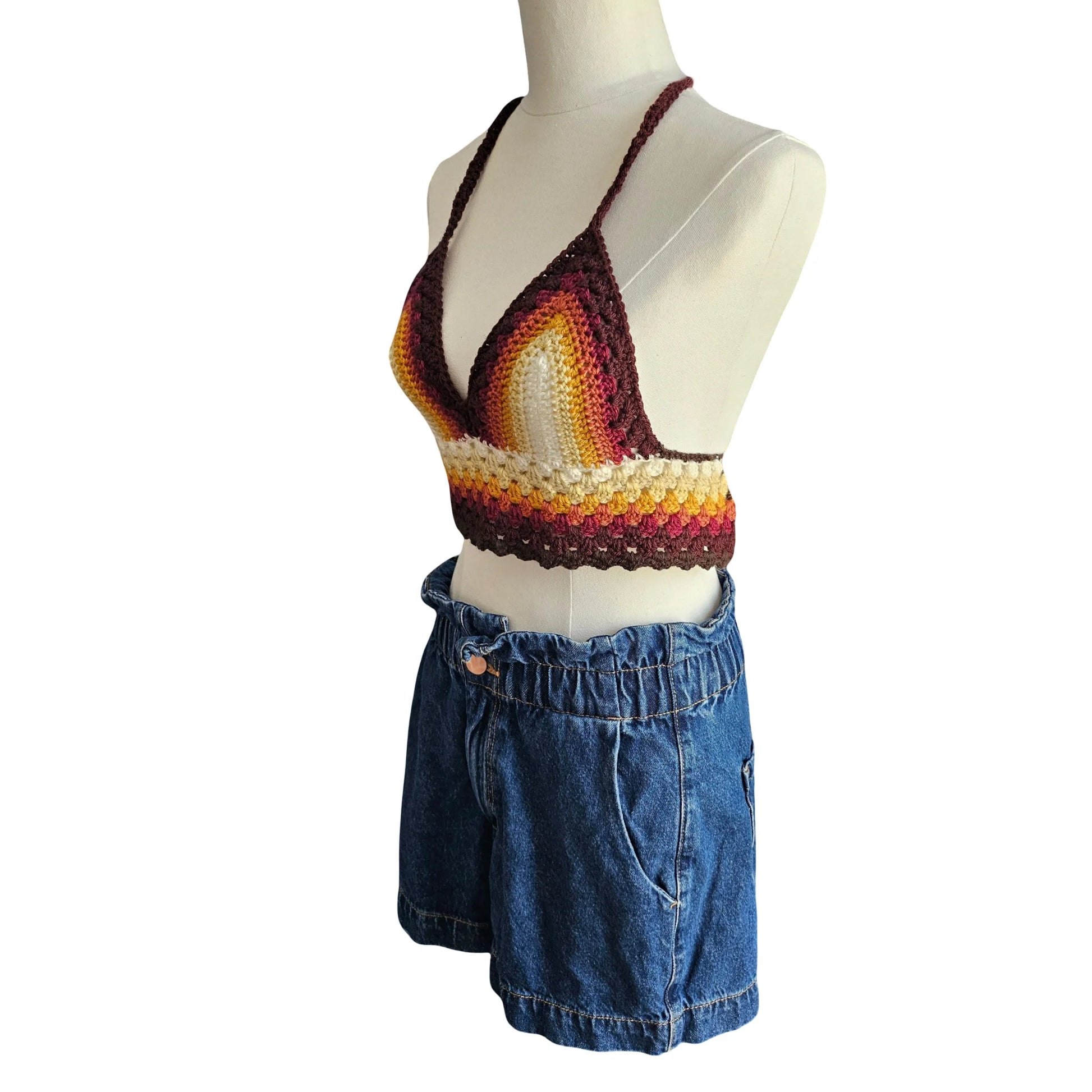 Colorful crochet top and blue denim shorts on a mannequin against a white background