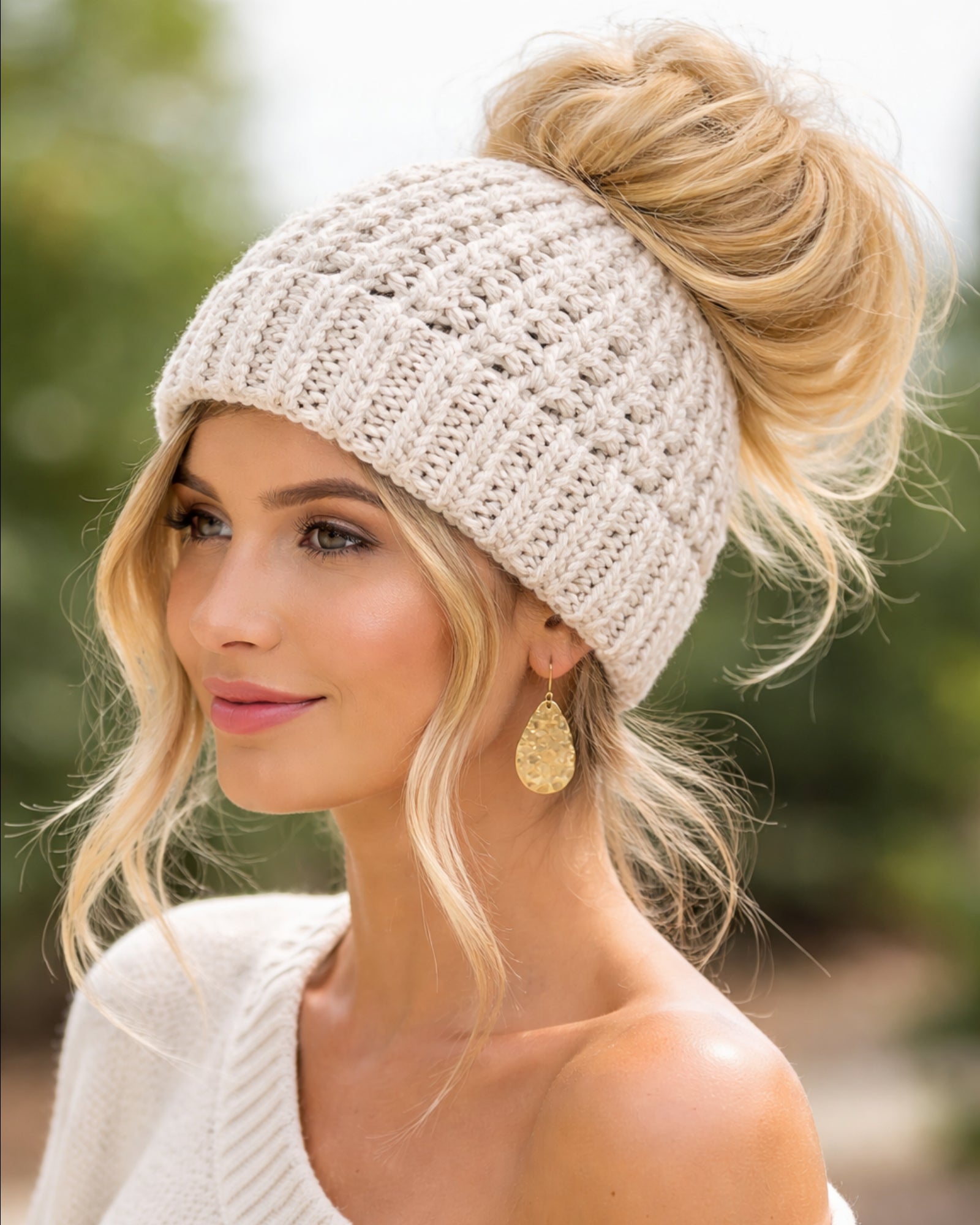 Woman wearing a beige knit beanie with her hair styled in a bun, outdoors.