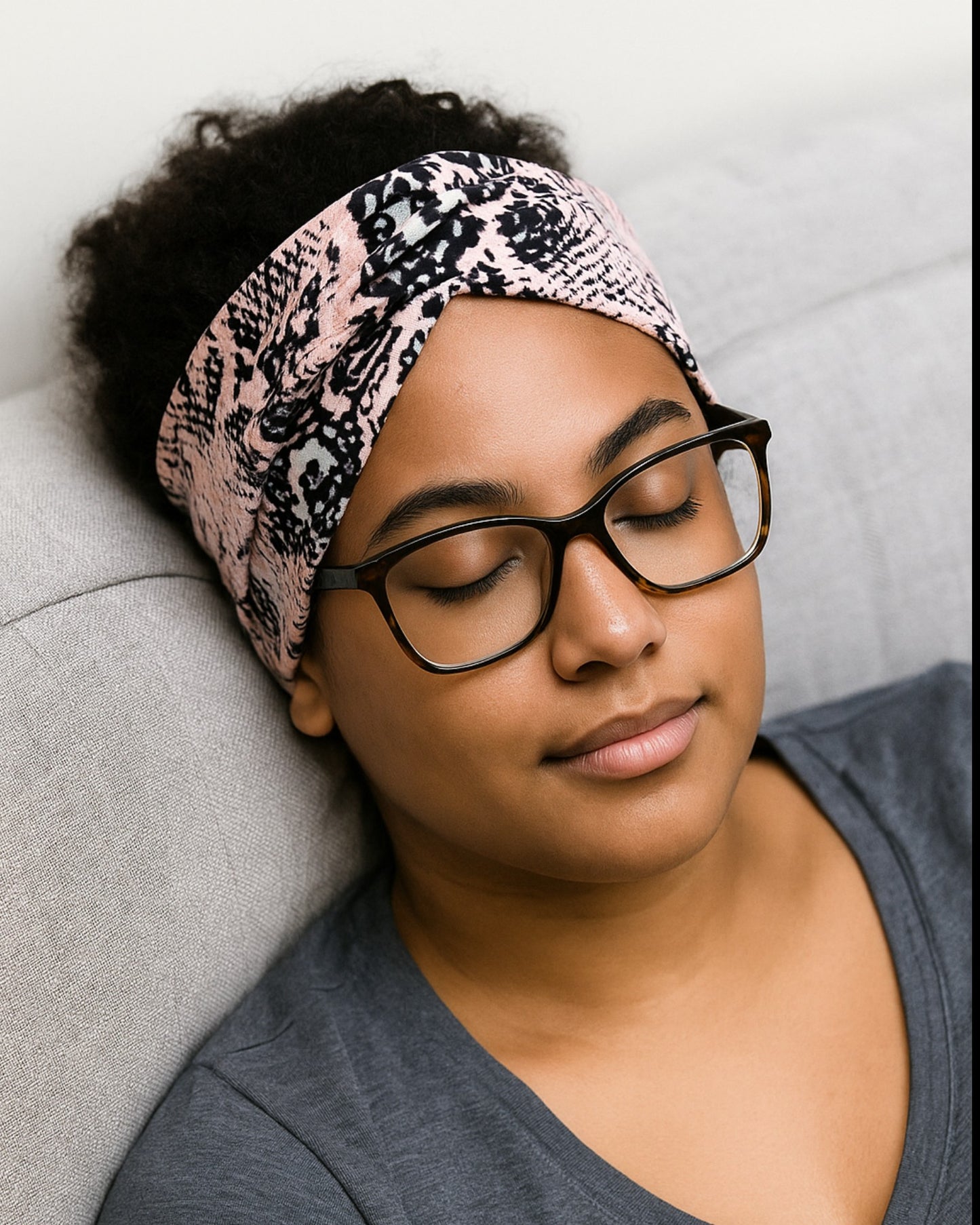 Woman wearing a patterned headband and glasses, sitting on a couch.